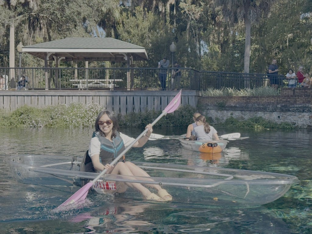 A guest smiling in a clear kayak and holding a pink paddle