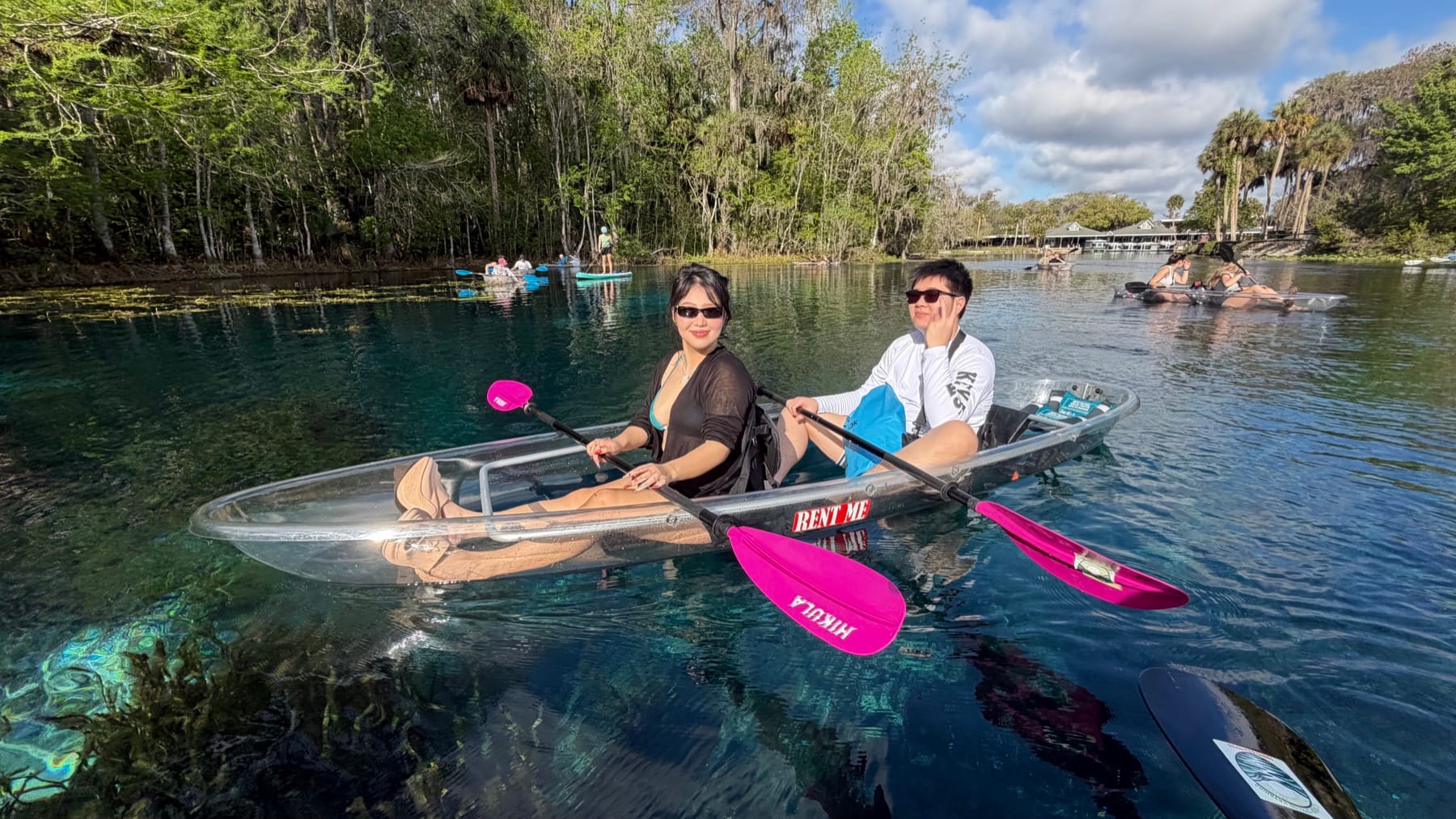 Two guests paddling a transparent tandem kayak with pink paddles on a Florida spring