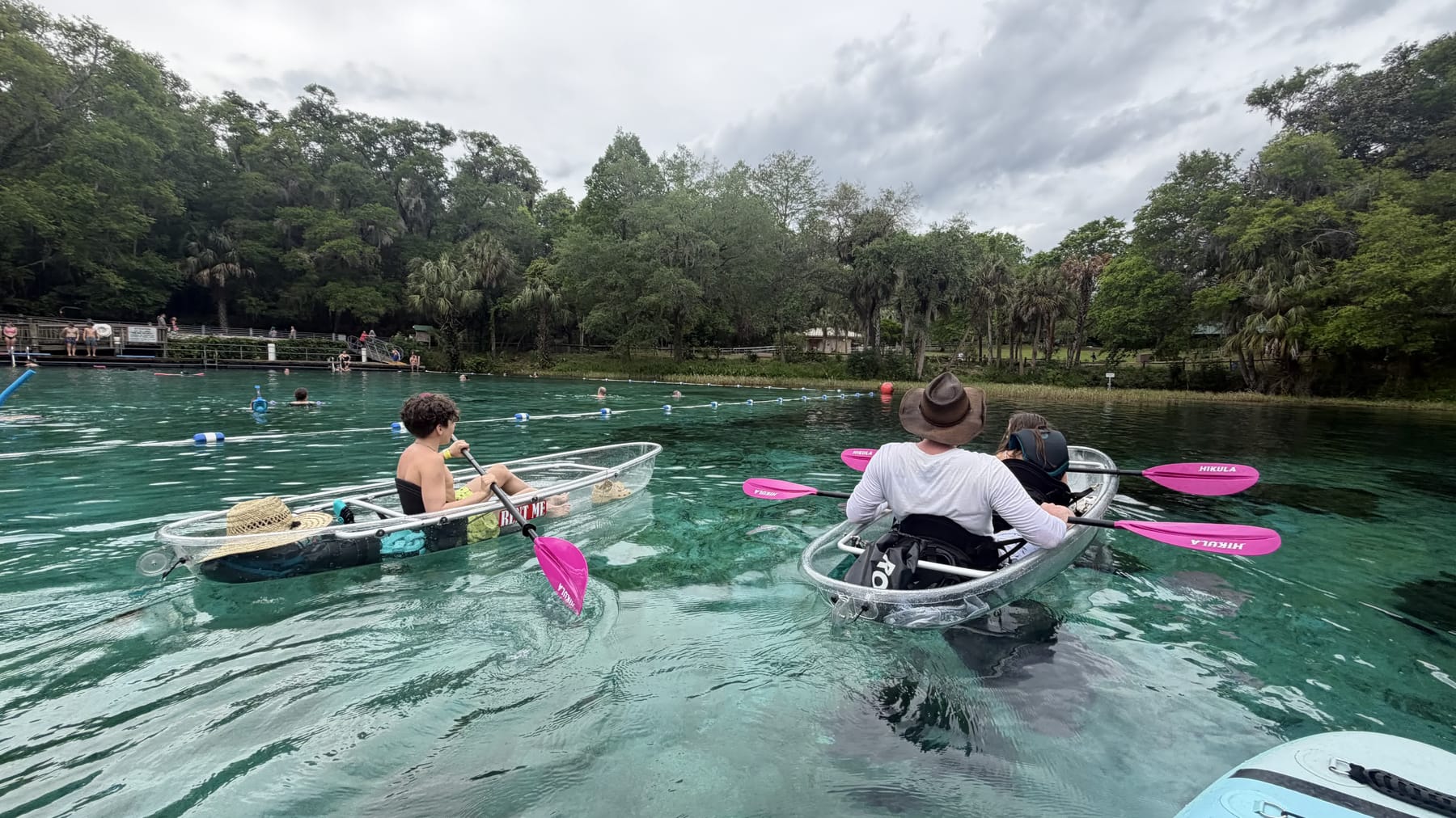 Clear kayaks heading out from a spring boardwalk on bright water
