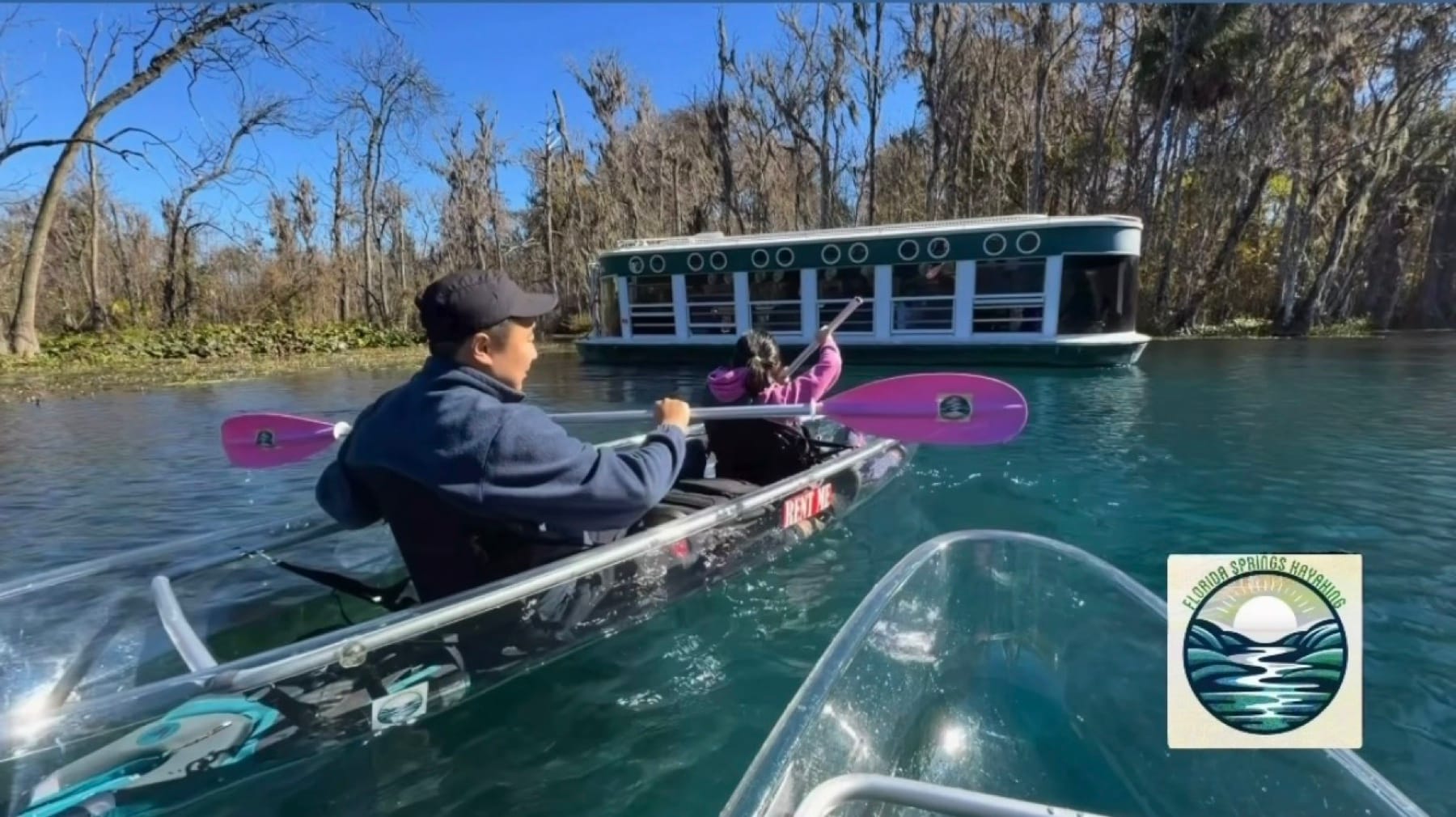 A tandem clear kayak paddling past a historic Silver Springs glass-bottom boat