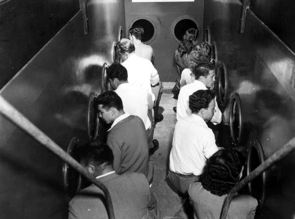 Visitors in 1956 leaning toward circular portholes inside a Rainbow Springs scenic submarine